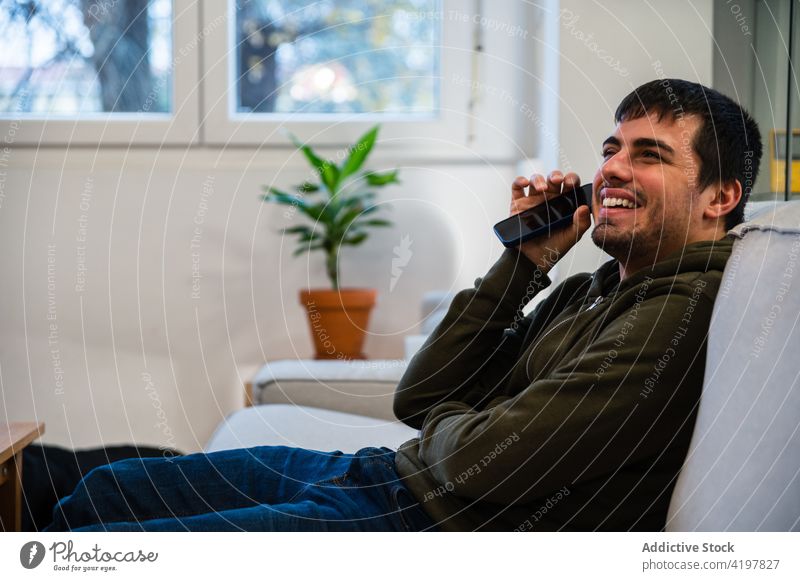 Cheerful blind man listening audio sitting on sofa using audio message disability smartphone positive enjoy communicate male carefree connection digital