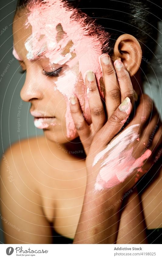 Ethnic woman with paint on face in studio model creative art fashion eccentric appearance female ethnic smear smudge stroke color dye style unusual touch cheek