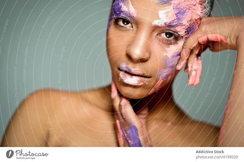 Ethnic woman with paint on face in studio model creative art fashion eccentric appearance female ethnic smear smudge stroke color dye style unusual unemotional