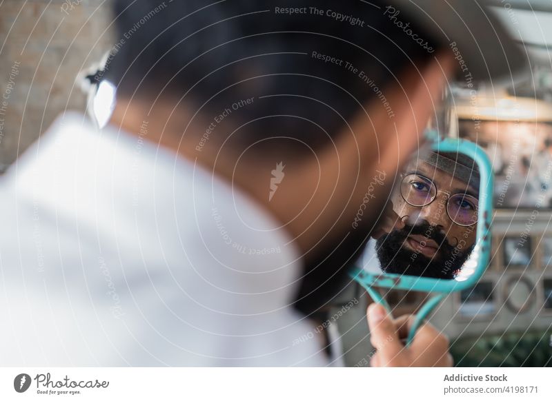 Crop ethnic barber looking in mirror in hairdressing salon reflection mustache hipster masculine brutal macho man curl professional beard serious rectangular