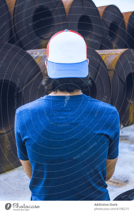 Anonymous man standing near steel rolled coils in industrial area metal factory alone style storage stack manufacture industry material male young dark hair