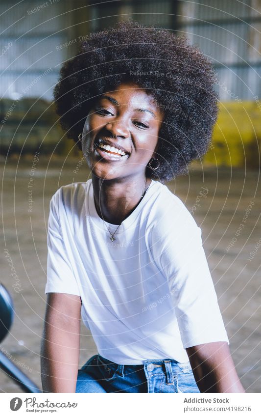 Confident young black woman smiling while sitting in hangar smile cheerful rest confident happy industrial style joy positive glad modern female