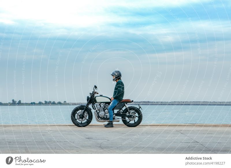 Anonymous guy sitting on motorbike and admiring sea man motorcycle embankment relax style cool construction biker recreation admire seaside male young casual
