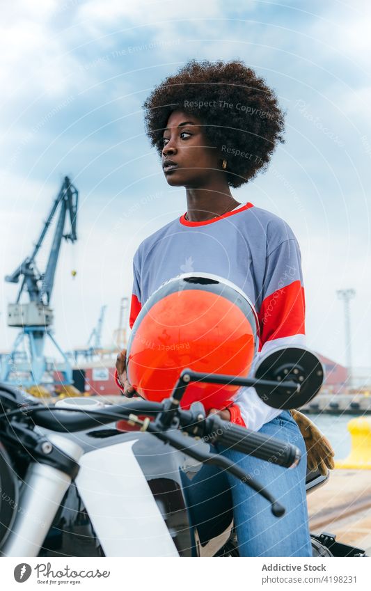 Serious young ethnic woman wearing helmet while sitting on motorbike motorcycle seaside appearance personality trendy embankment alone biker cool travel vehicle