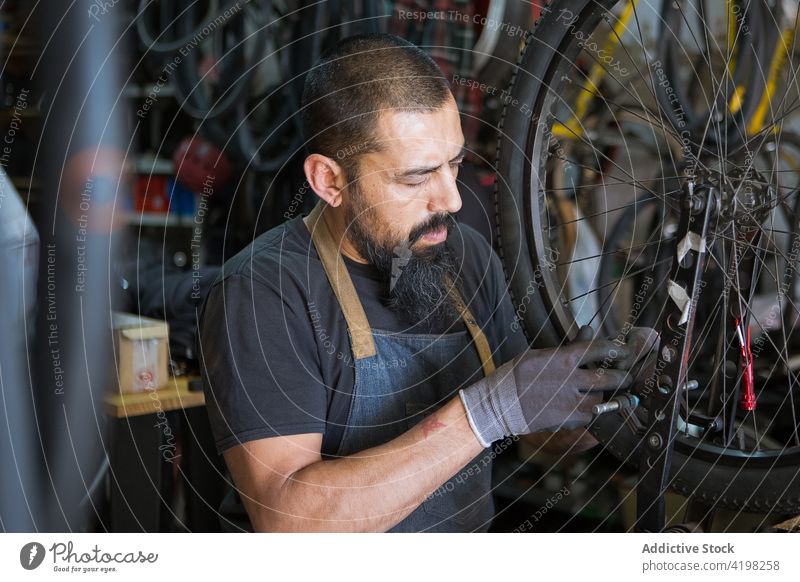 Bearded mechanic repairing wheel of bicycle man garage tire workshop service master skill male vehicle prepare bike professional tool handyman concentrate