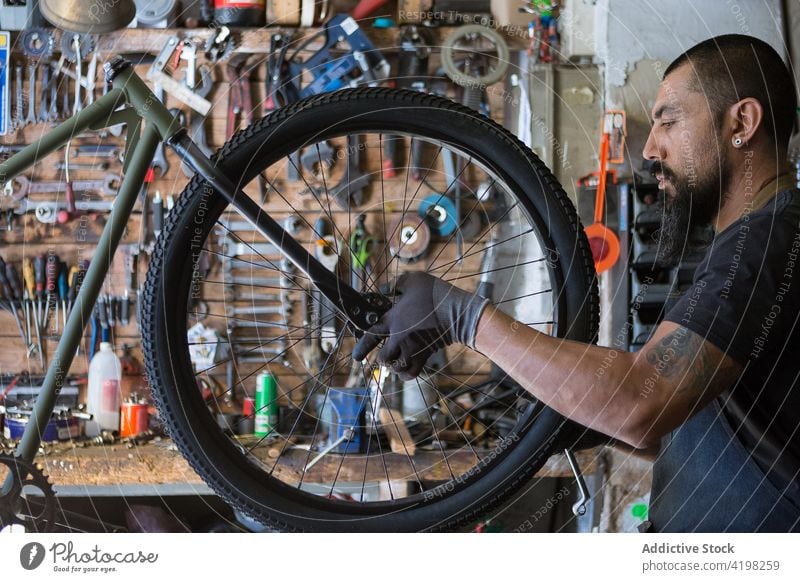 Bearded mechanic repairing wheel of bicycle man garage tire workshop service master skill male vehicle prepare bike professional tool handyman concentrate