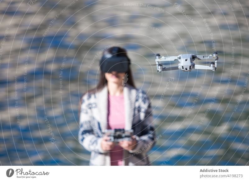 Cheerful woman in VR glasses operating drone at seaside vr operate virtual reality flight remote control female fly unmanned controller device gadget excited