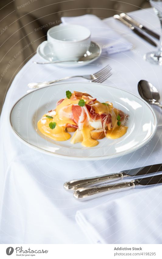 Delicious poached egg with bacon and sauce served on table during breakfast benedict coffee silverware brunch appetizing dish meal tasty restaurant plate cup