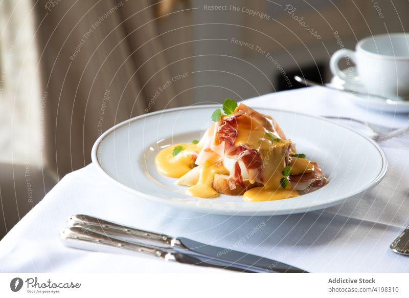 Delicious poached egg with bacon and sauce served on table during breakfast benedict coffee silverware brunch appetizing dish meal tasty restaurant plate cup