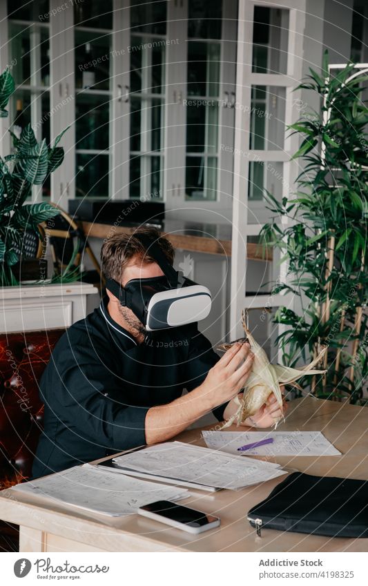 Anonymous man using VR goggles while sitting in restaurant with corn and documents vr experience work virtual reality digital simulate headset technology male