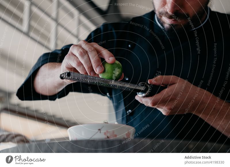 Anonymous male chef adding ingredient to meal while cooking at restaurant man grater rub zest process culinary fruit counter prepare kitchen food recipe lunch