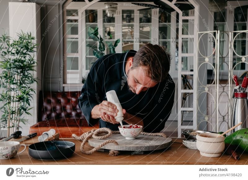 Focused man decorating dessert with cream in stylish restaurant decorate chef berry delicious cook concentrate job culinary prepare male young beard uniform