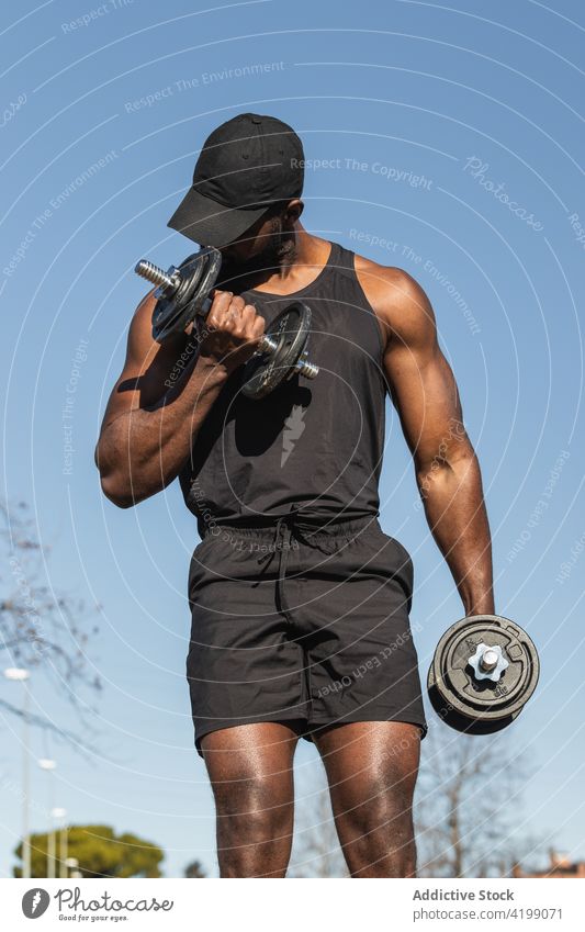 Unrecognizable black sportsman with dumbbells during training in city athlete workout fitness muscular body town weight equipment sportswear masculine macho
