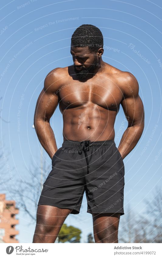 Strong ethnic sportsman resting during training on sports ground workout naked torso strong muscular wellness hand on hip shirtless abdomen hipster wellbeing