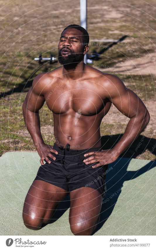 Strong ethnic sportsman breathing during training on sports ground breathe workout naked torso eyes closed strong muscular wellness hand on hip shirtless