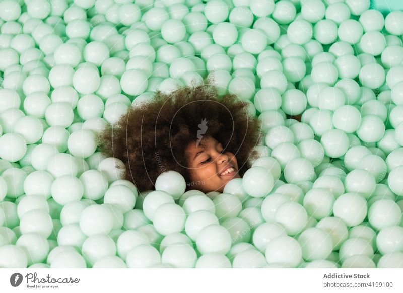 Cheerful child in ball pit play cheerful pool plastic happy afro hairstyle ethnic black african american kid fun childhood having fun enjoy content glad cute