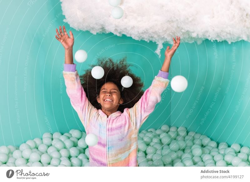 Excited black girl playing in ball pit having fun throw toss delight excited playful ethnic african american entertain pool carefree child enjoy game cheerful