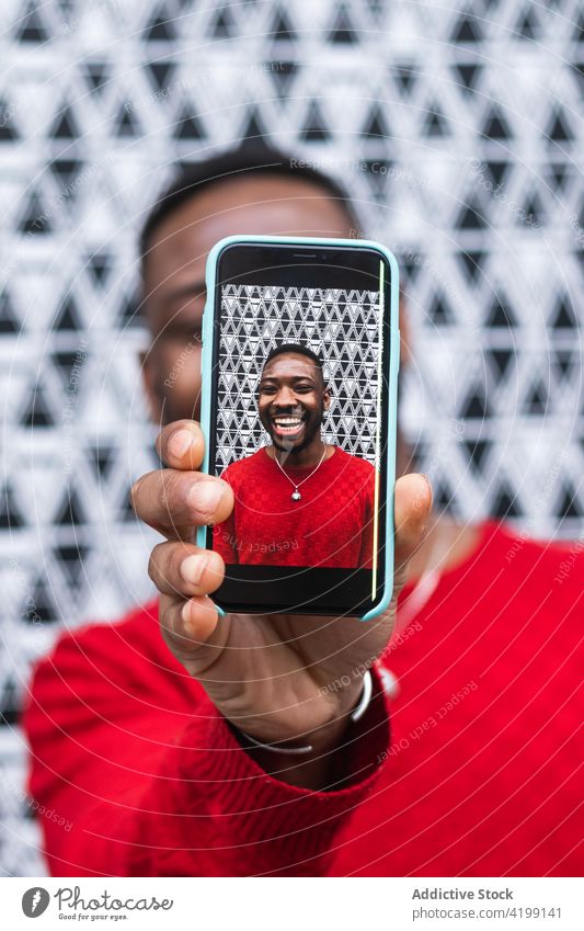 Black man showing photo on smartphone screen cheerful sincere cover face macho friendly using gadget device masculine bright african american black cellphone