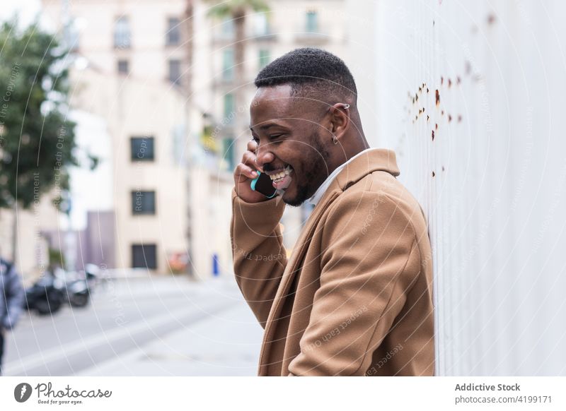 Well dressed happy black man on a phone call on smartphone near wall speak internet masculine cheerful macho using gadget device african american ethnic chat