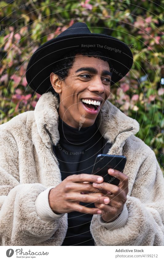 Stylish happy ethnic man with smartphone on street enjoy trendy wireless using gadget device internet online cellphone hat garment fashion style masculine male