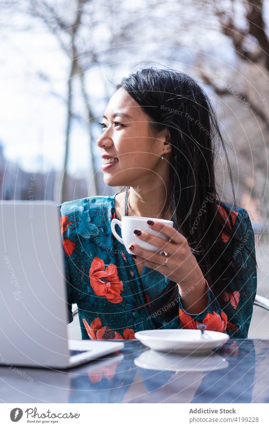 Long-haired brunette Asian woman having a coffee on a terrace of a cafe while is working with a laptop asian people shop female chinese computer coffee shop cup