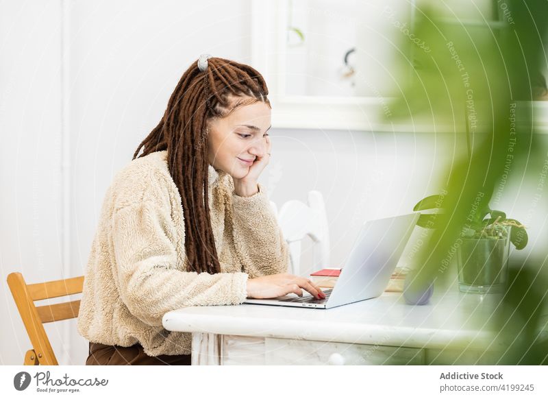 Thoughtful woman with dreadlocks working with a laptop at home computer sitting room internet female technology people lifestyle young girl house modern