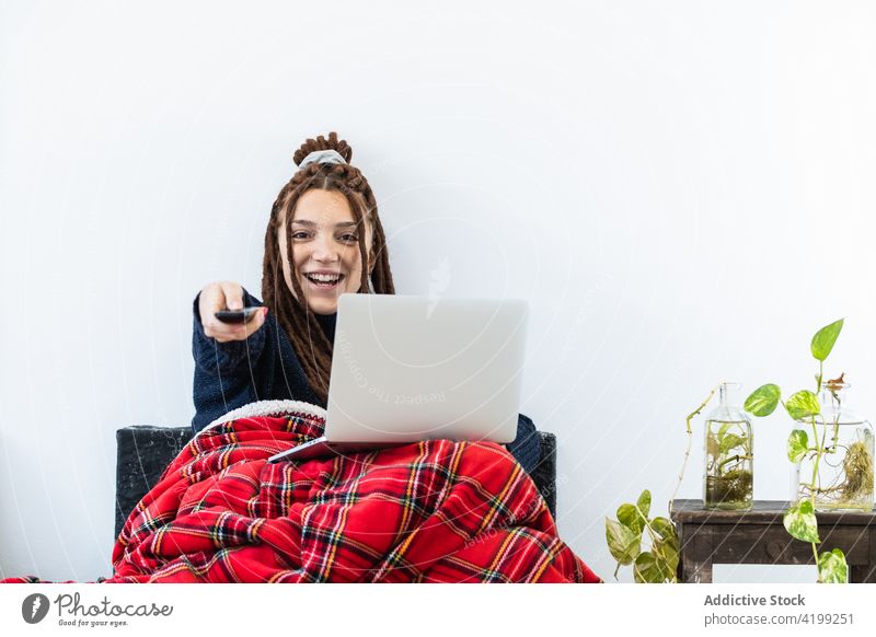 Woman with dreadlocks working with a laptop at home and with a remote control in hand woman computer sofa sitting room internet female technology people