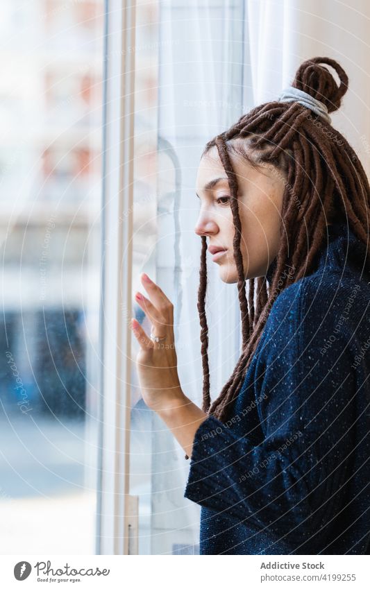 Pensive woman with dreadlocks looking out the window pensive home people thinking braids contemplation beautiful portrait person adult lifestyle face female