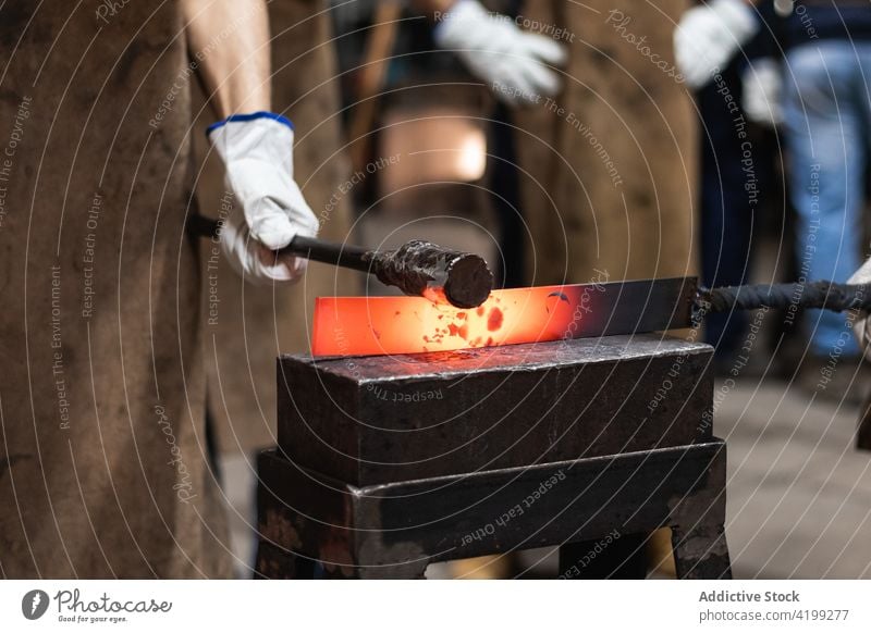 Blacksmith in gloves hot hitting metal part on anvil man blacksmith iron process hammer tool fabricate male workshop job artisan metalwork production