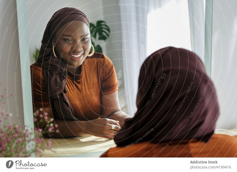 Happy young ethnic female looking in mirror in modern room woman style reflection elegant appearance fashion personality trendy calm serene black african muslim