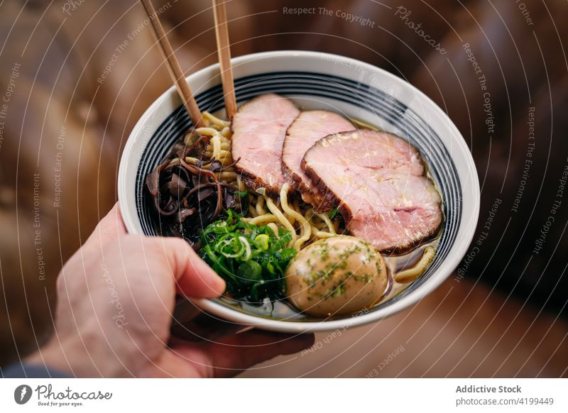 Crop man with bowl of ramen soup chopstick restaurant dish eat asian food ham tasty male meal palatable yummy culinary portion delicious piece cuisine