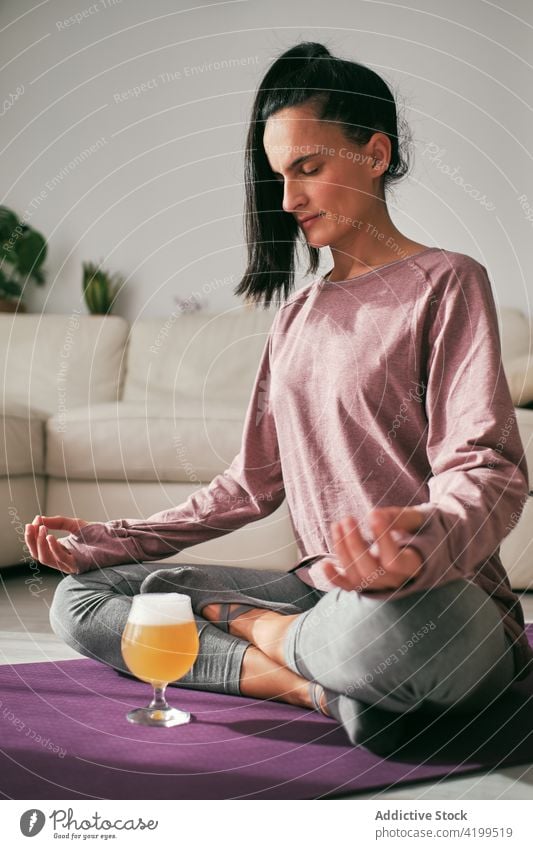 Woman doing yoga with glass of beer at home woman lotus pose meditate brew padmasana serene mudra female mat relax wellness device calm laptop healthy zen