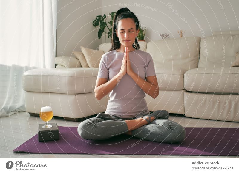 Woman doing yoga with glass of beer at home woman lotus pose meditate brew padmasana serene mudra female mat relax wellness device calm laptop healthy zen