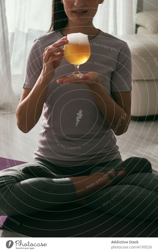 Crop woman in Lotus pose with glass of beer yoga lotus pose drink alcohol padmasana practice home female mat wellbeing beverage sit vitality harmony healthy