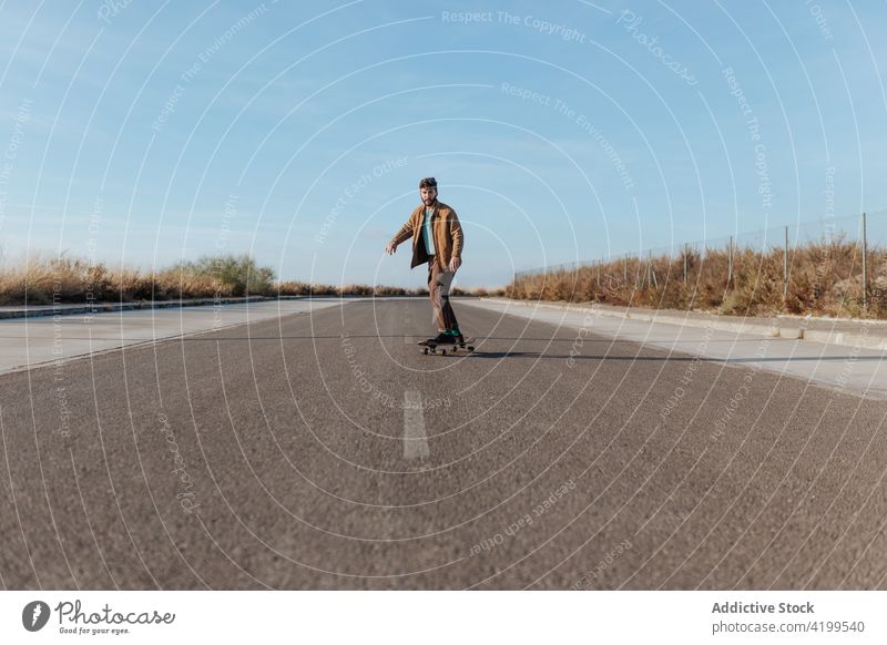 Young bearded skater on asphalt road man ride skateboard countryside rural nature hobby subculture practice skill male energy cool motion sport balance move
