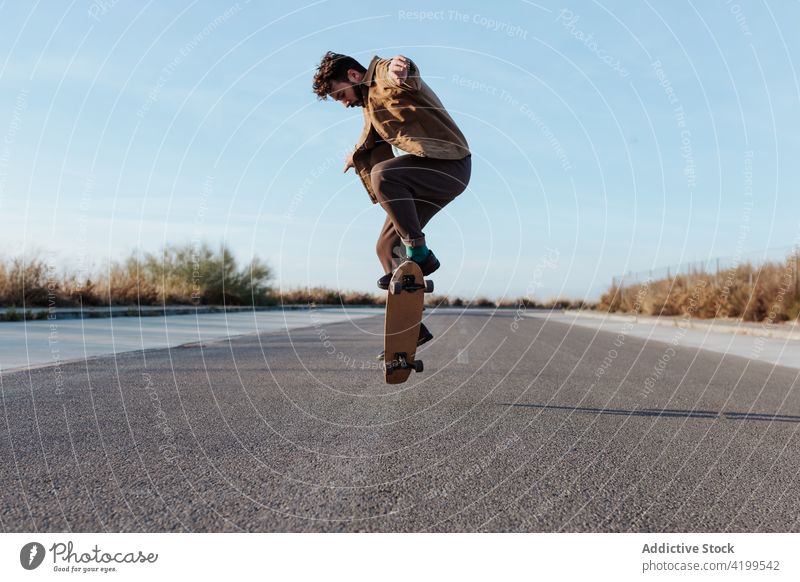 Energetic young skater performing trick on skateboard man kickflip jump stunt energy skill road countryside nature rural male motion activity hobby sport