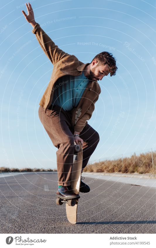 Trendy skater keeping balance standing on skateboard man trick nature perform edge skill countryside rural hobby road male asphalt practice sport subculture
