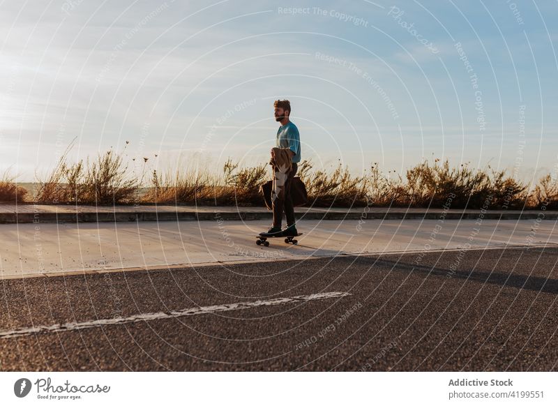 Relaxed stylish skater riding skateboard along pavement man ride freedom relax trendy style nature rural countryside peace road asphalt skill hobby activity