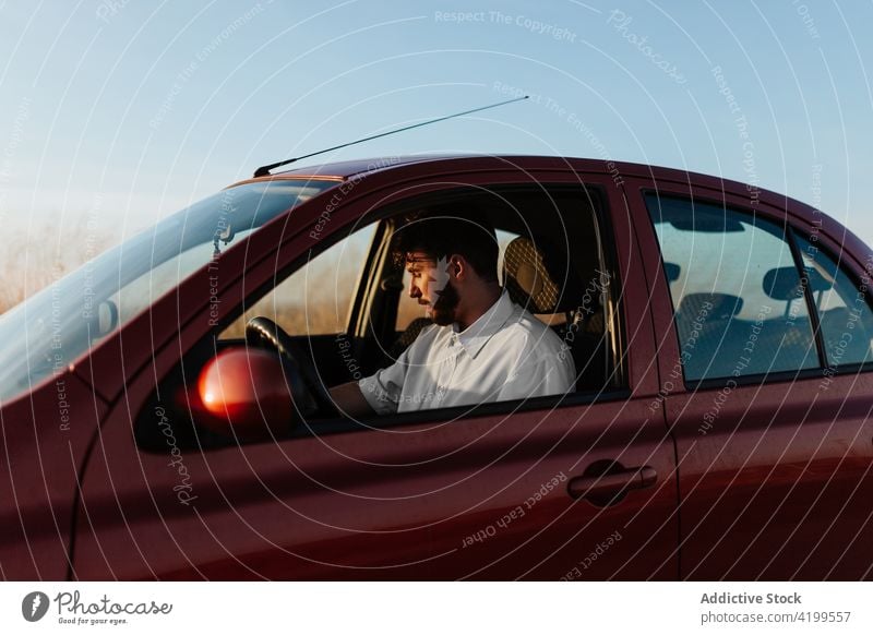 Bearded young man sitting in car in nature drive parked roadside vehicle transport automobile countryside road trip journey male travel casual white shirt beard