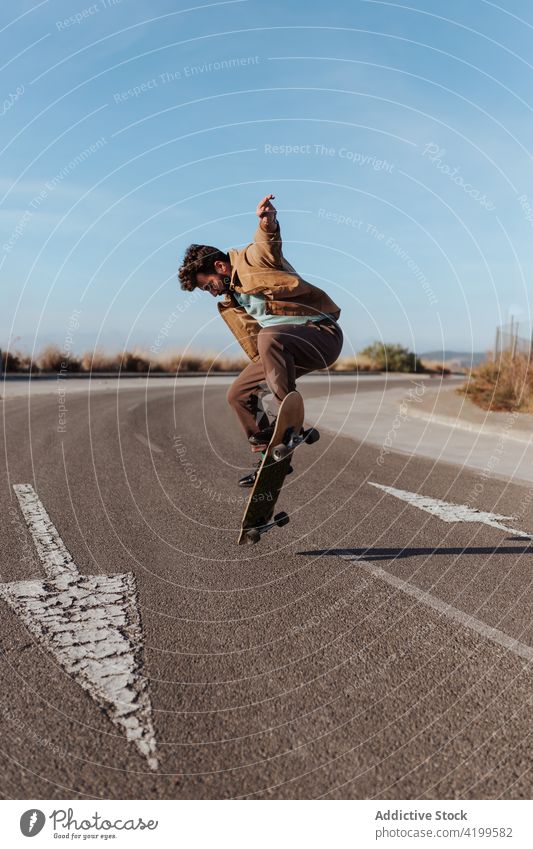 Energetic young skater performing trick on skateboard man kickflip jump stunt energy skill road countryside nature rural male motion activity hobby sport