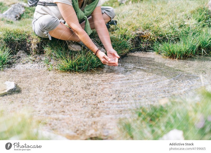 Anonymous woman washing hands in brook in stony terrain nature backpacker creek peaceful rest sit harmony travel adult meadow casual female sunny pyrenees spain