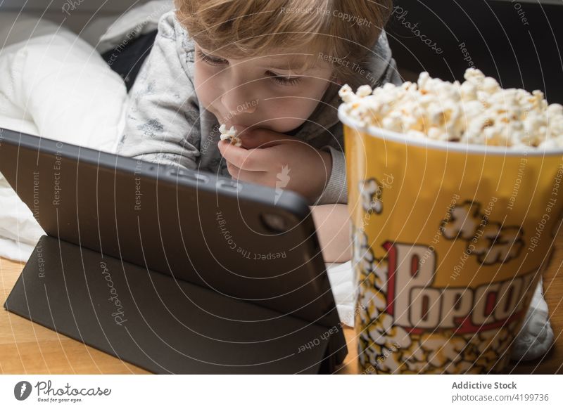 Child on the couch watching tv on tablet and eating popcorn kid boy enjoy film having fun cartoons lifestyle movie sofa children snack little living room