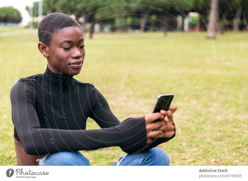 Charming black woman with headphones taking selfie on smartphone self portrait african american ethnic sitting grass park charming cellphone photo using gadget