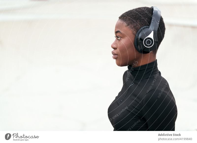Dreamy black woman in headset resting on platform short hair headphones music listen reflective dreamy trendy song portrait using device wireless profile ripped