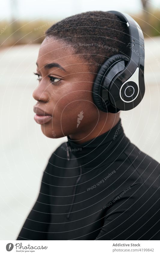Dreamy black woman in headset resting on platform short hair headphones music listen reflective dreamy trendy song portrait using device wireless profile ripped
