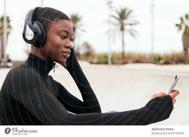 Smiling black woman in headset watching smartphone on street african american song listen short hair content internet portrait using gadget town device browsing