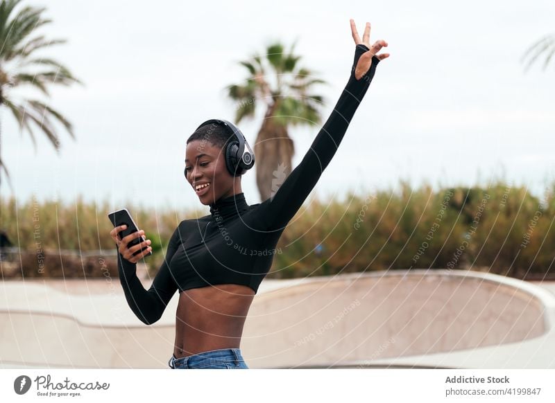Smiling black woman in headset watching smartphone on street african american song listen short hair content internet portrait using gadget town device browsing