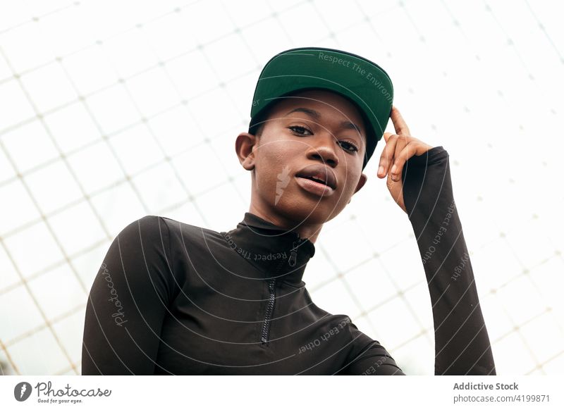 Cool black woman in cap against grid fence individuality cool style finger up trendy city portrait wear casual garment gentle modern cloth african american