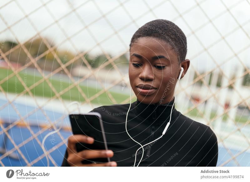 Attentive black woman in earphones chatting on smartphone in town short hair music watching listen internet portrait using gadget attentive cellphone device