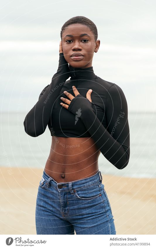Trendy black model touching chest and face on sea shore woman short hair seashore style sensitive touch cheek belly touch chest gentle portrait trendy tender